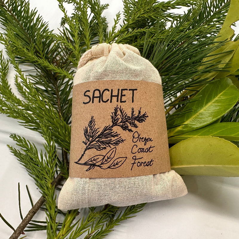 Sachet bag with 'Oregon Coast Forest' text and design, surrounded by green foliage on a white background