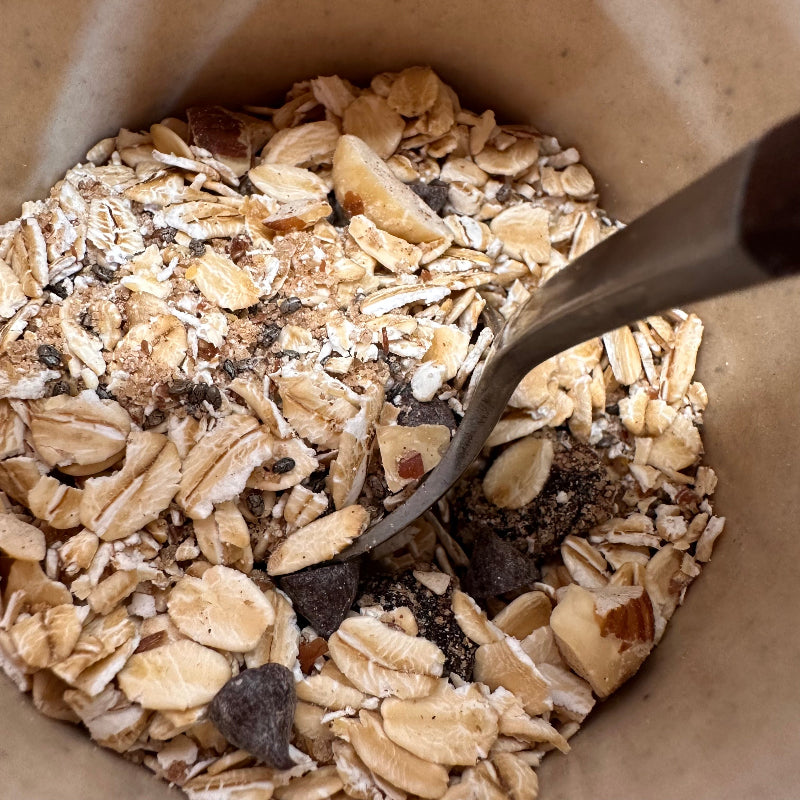 Close-up of instant oats with dried fruit, nuts and chocolate pieces in a brown mug with a spoon.
