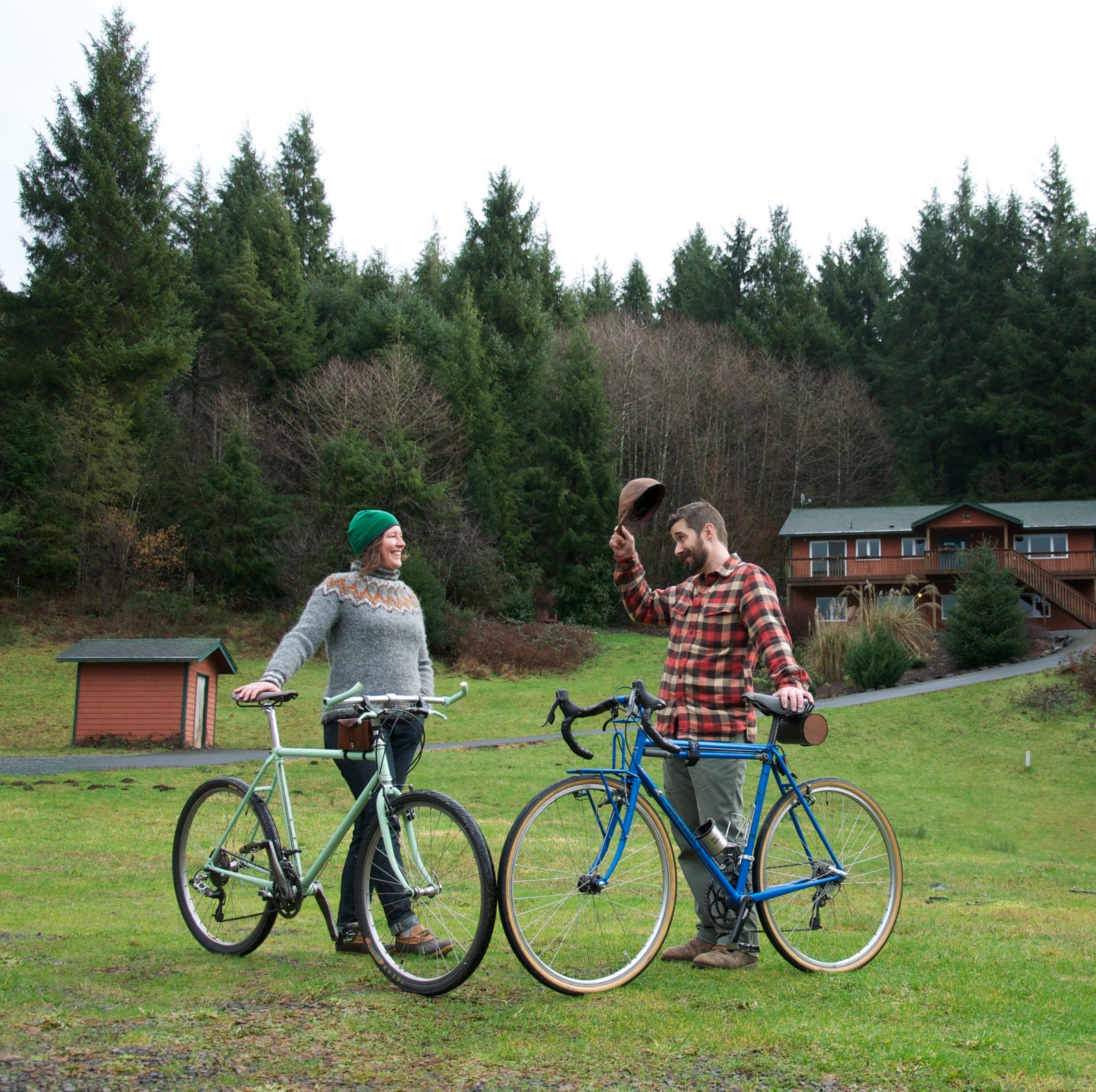 Valerie and Geoff Franklin of Walnut Studiolo standing behind their bicycles on a grassy green lawn. Geoff is doffing his hat to Valerie and she is smiling, as a gesture of service.