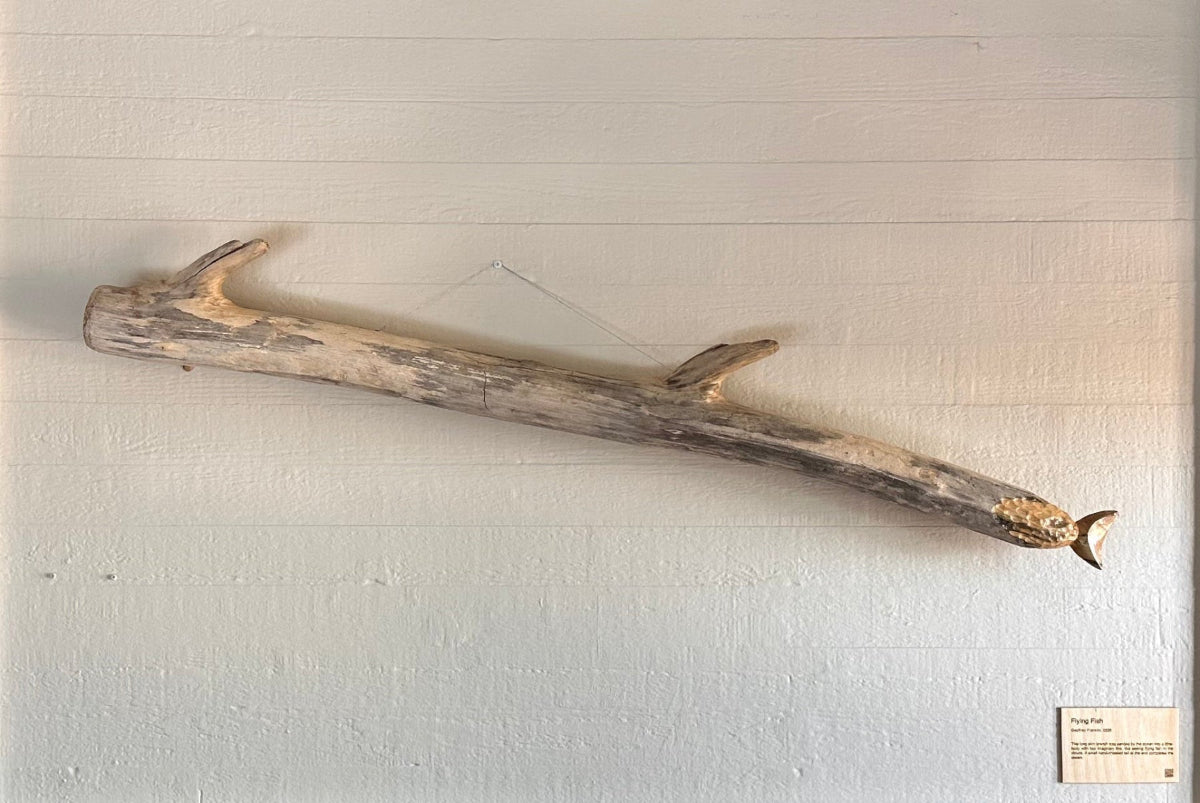 White fireplace with a large driftwood branch sculpture shaped with a fish tail and fins on the mantel in a room with neutral walls.