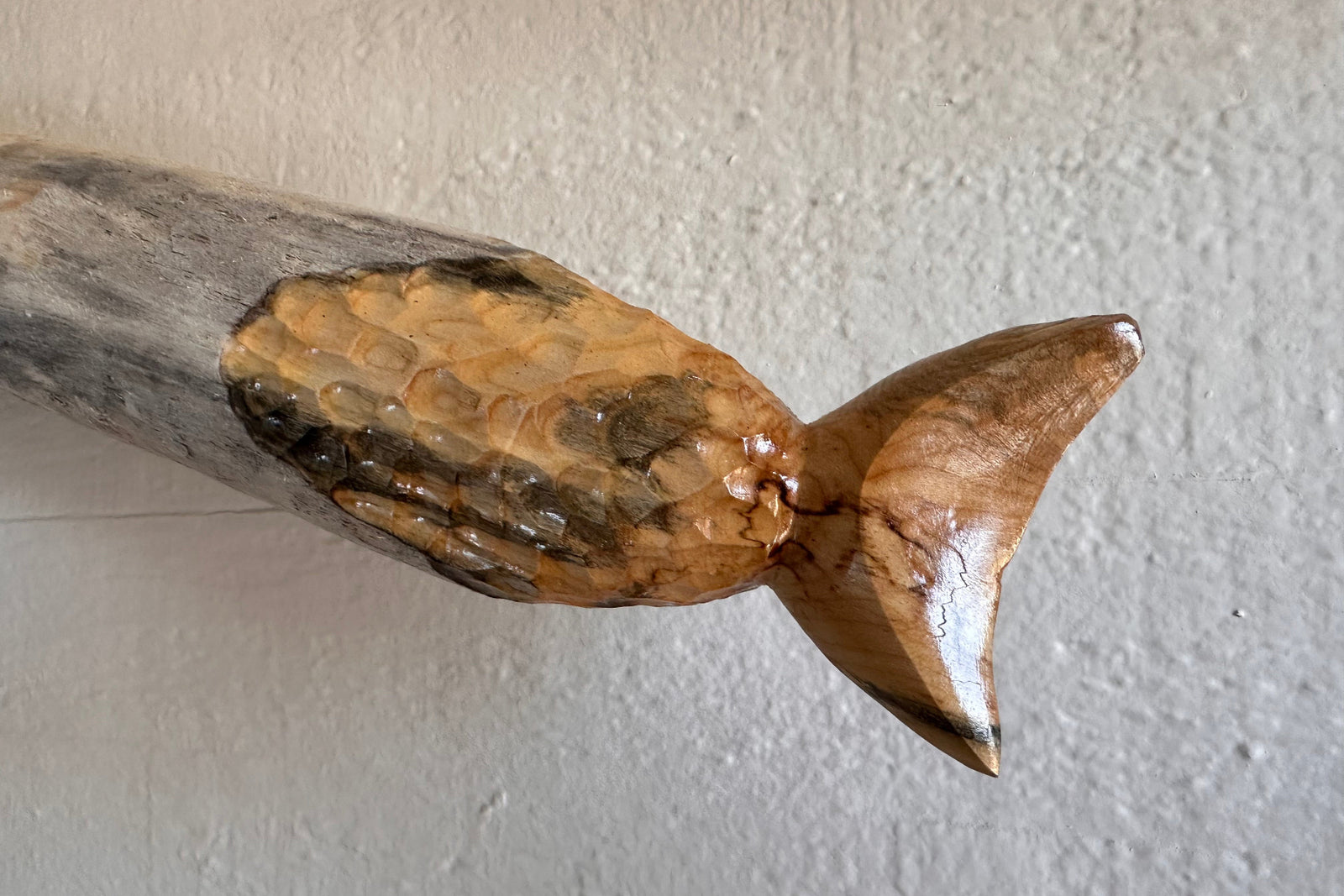 Close-up detail of a wooden fish sculpture on a textured white background
