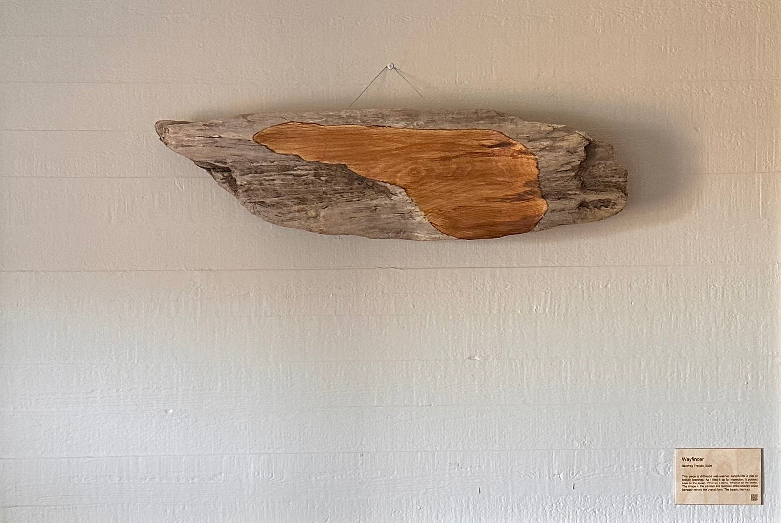 White wall with a fireplace and a piece of driftwood art above it
