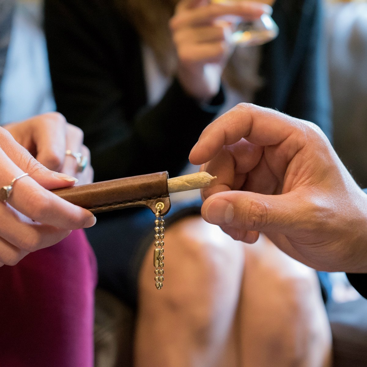 A woman is passing a leather tube with a brass ball chain keyring towards a man, who reaches for a handroll from inside the tube
