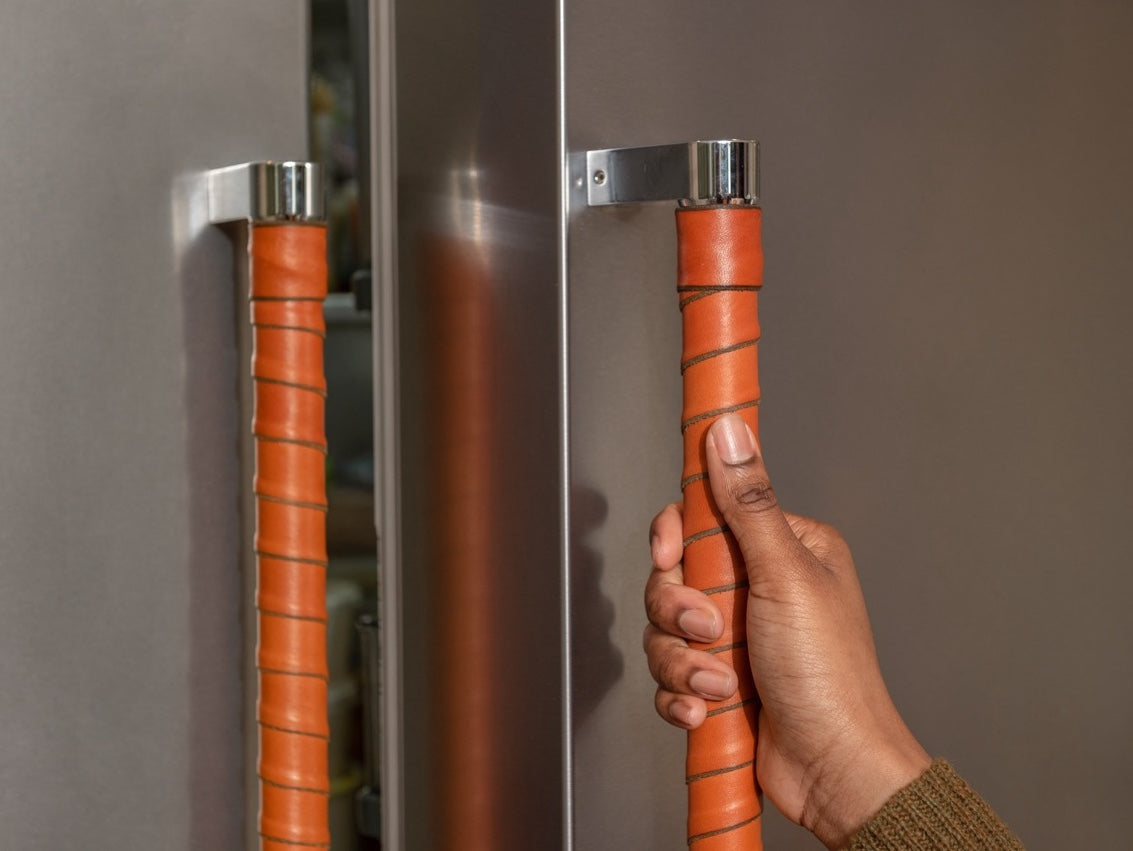 Person holding a refrigerator door handle with a beautiful and eye-catching honey brown leather wrap