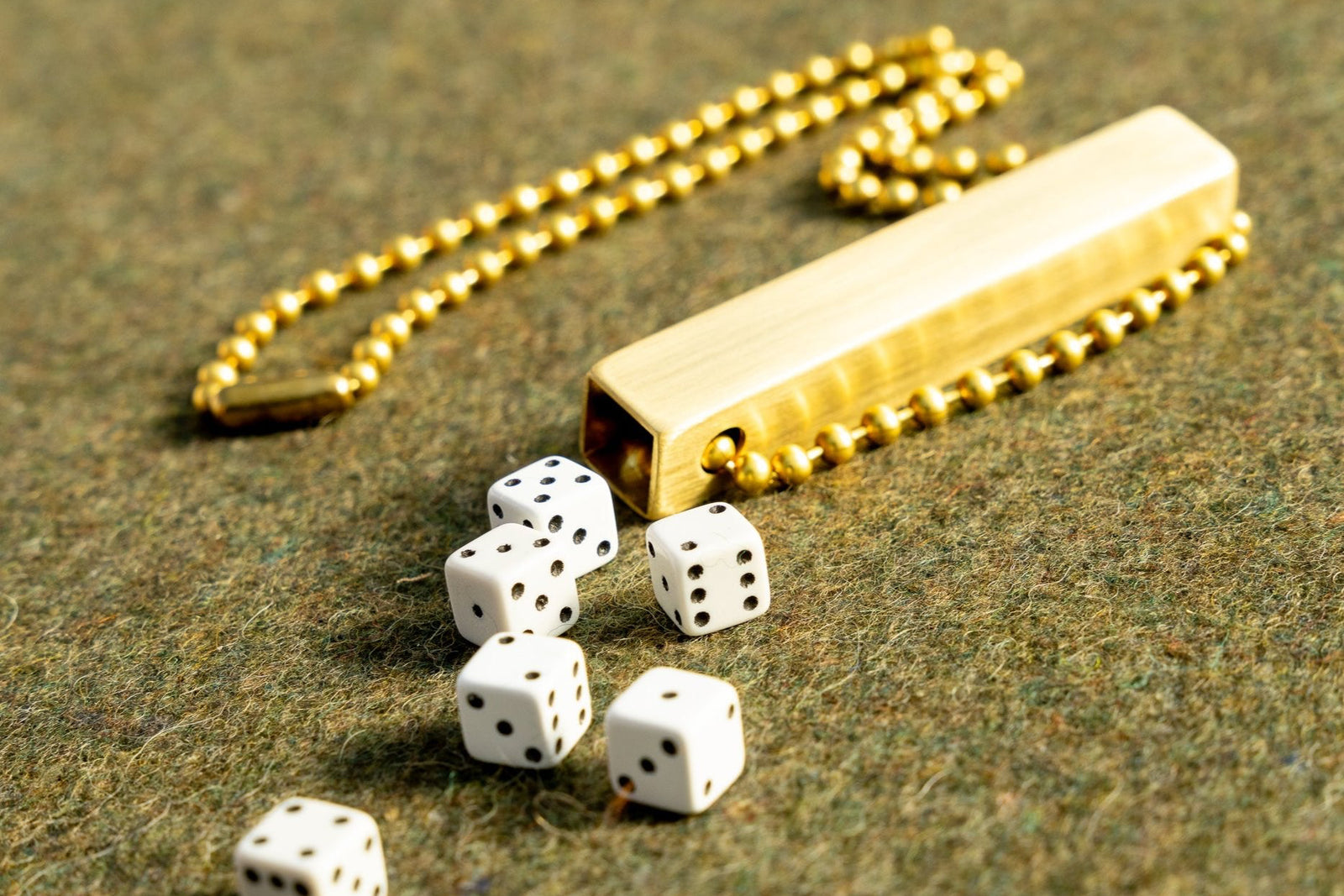 white travel dice in a brass tube with a necklace length beaded ball chain on a green wool army blanket