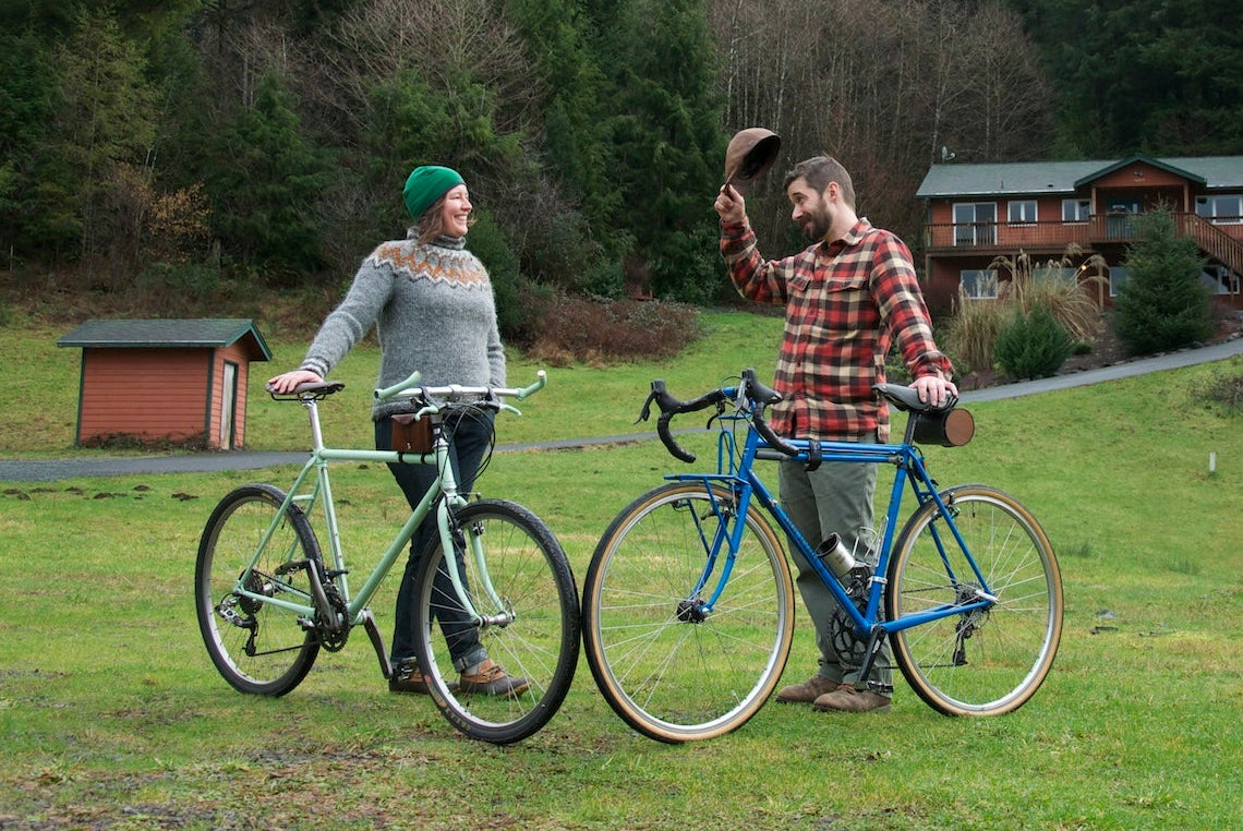 A man and a woman holding their bicycles upright while the man tips his cap to the lady in the Oregon coast forest