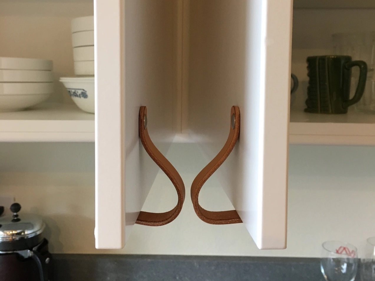 Two cabinet doors swinging open towards each other with matching leather Lovejoy loop handles. The leather touches so the cabinets don't crash into each other, a solution for problem corners in kitchen design planning