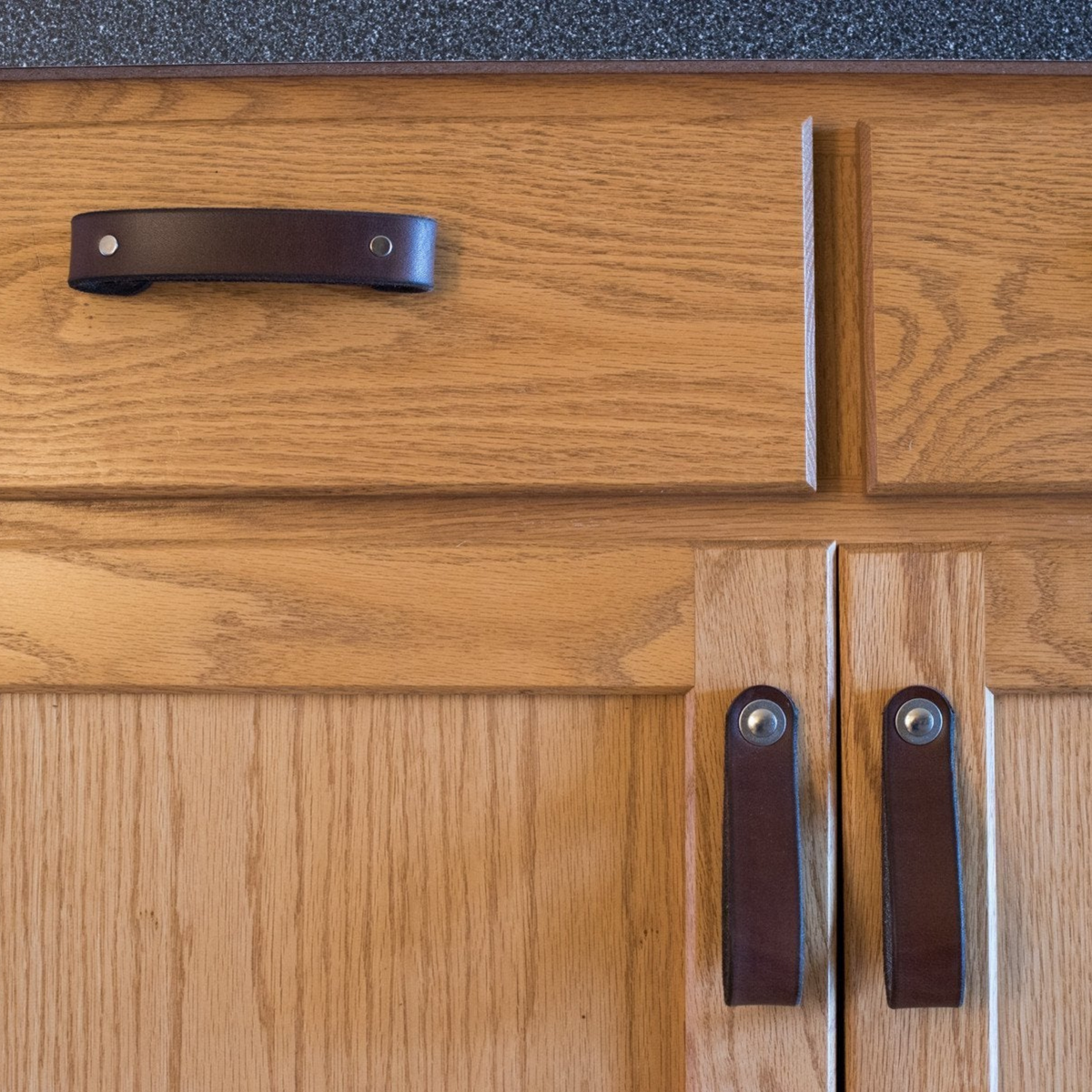 Close-up straight-on view: Dark Brown leather handles on an oak kitchen island. 