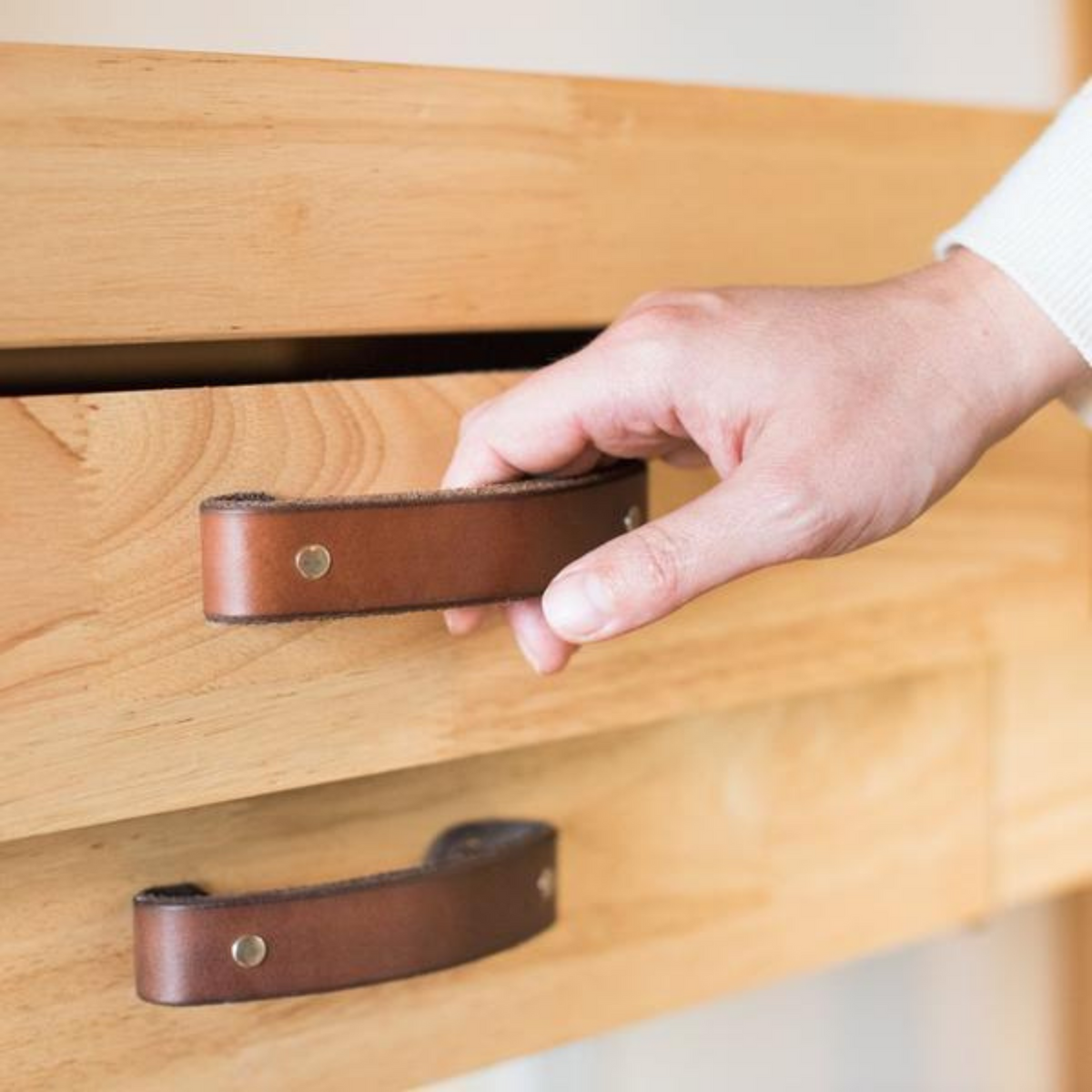 Woman&#39;s hand reaching towards a dark brown leather handle on a knotty pine buffet table drawer, which a Harbor Freight woodworking bench.