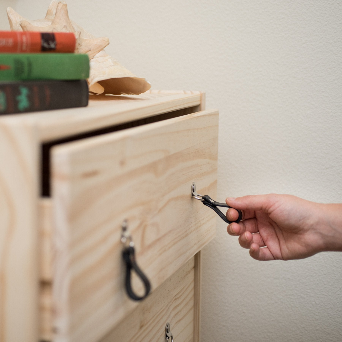 Woman&#39;s hand reaching out to an IKEA knotty pine wood dresser drawer and pulling it open using a small leather hinged handle in black leather with nickel hardware. 