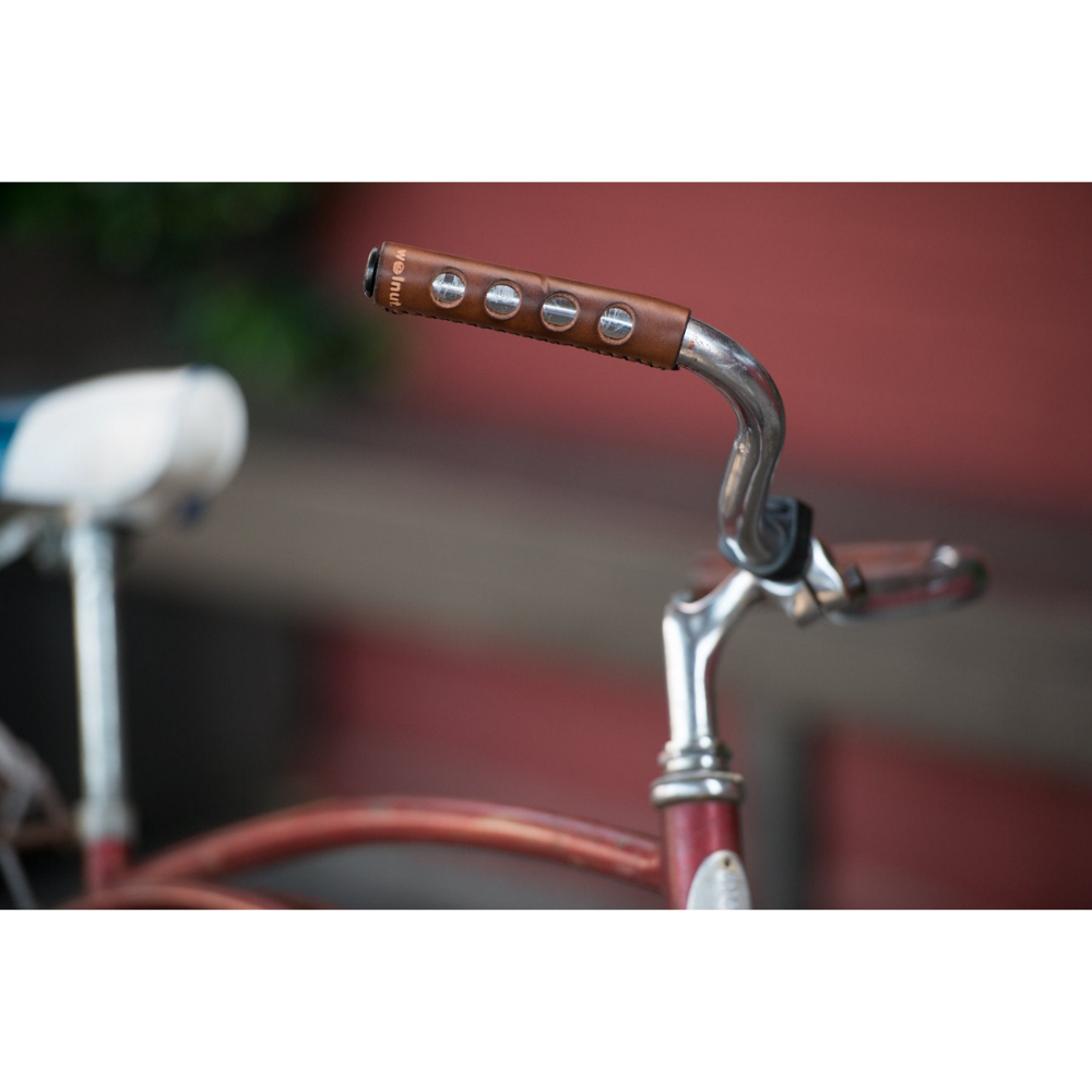 Old-fashioned steel Schwinn bicycle with a blue glitter saddle and curved red glitter top tube with a curvy handlebar that has dark brown leather grips sew-on. 