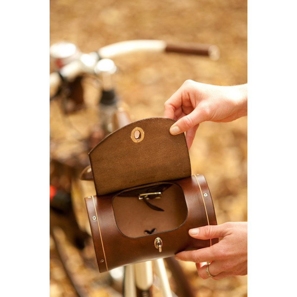 Hand opening dark brown leather barrel bag attached to saddle to demonstrate hole opening size