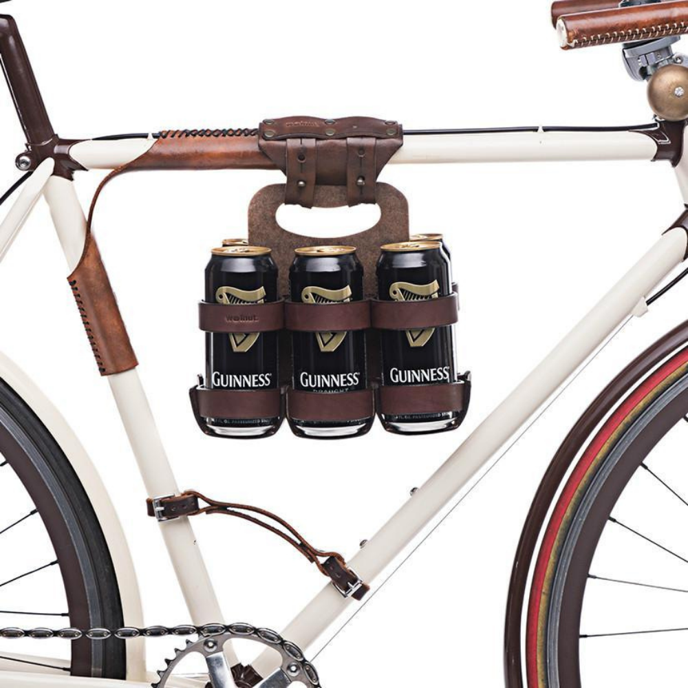 Close-up of dark brown leather beer hanger carrier hanging from the top tube of a white bicycle frame. The spartan carton beer holder is holding six 16 oz. beer cans. The little lifter bicycle handle is also featured in this product photo.