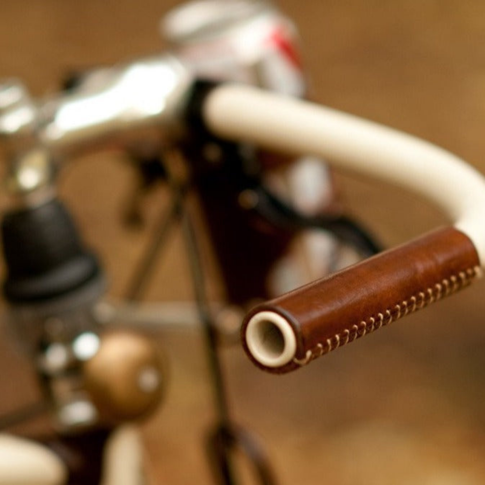 Close-up photo of a dark brown leather bicycle grip on a cream-painted bicycle handlebar