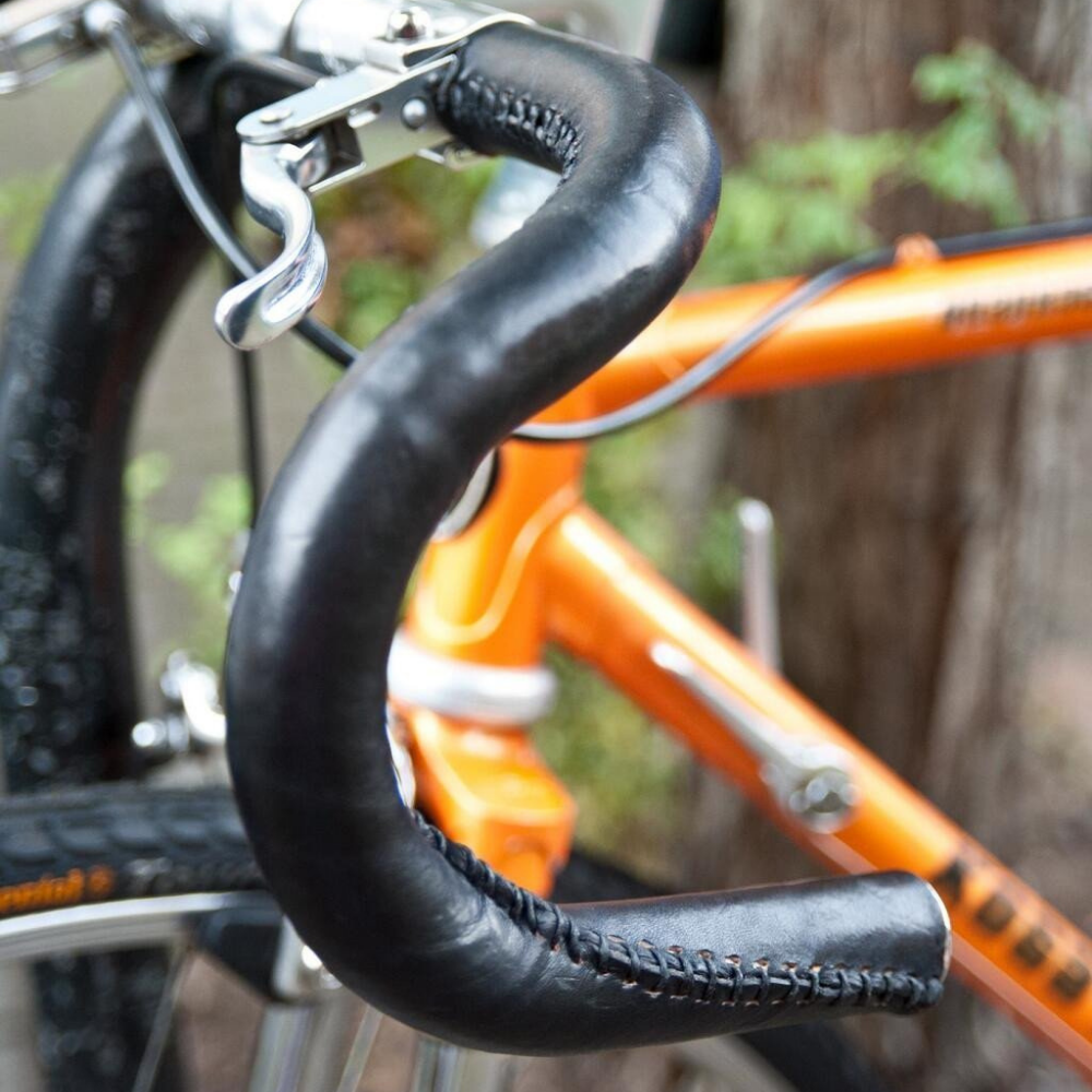 Customer photo of an orange steel frame bicycle with black leather sew-on bar wraps on handlebars in the rain. 