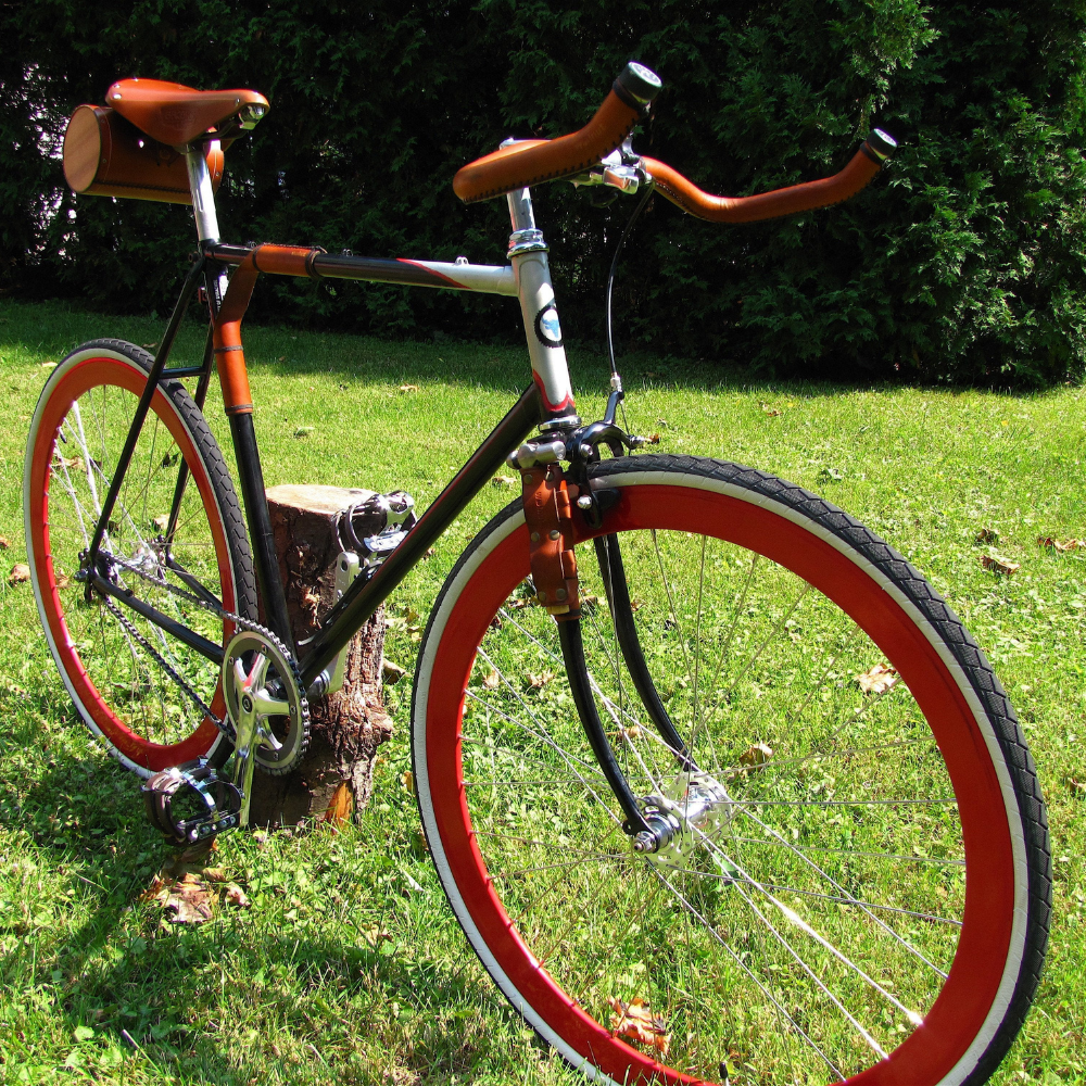 Customer bicycle photo of a red-and-black themed bicycle with honey leather sew-on bar wraps on bullhorn handlebars. The sew-on bar wraps were cut short to fit bullhorn bars. 