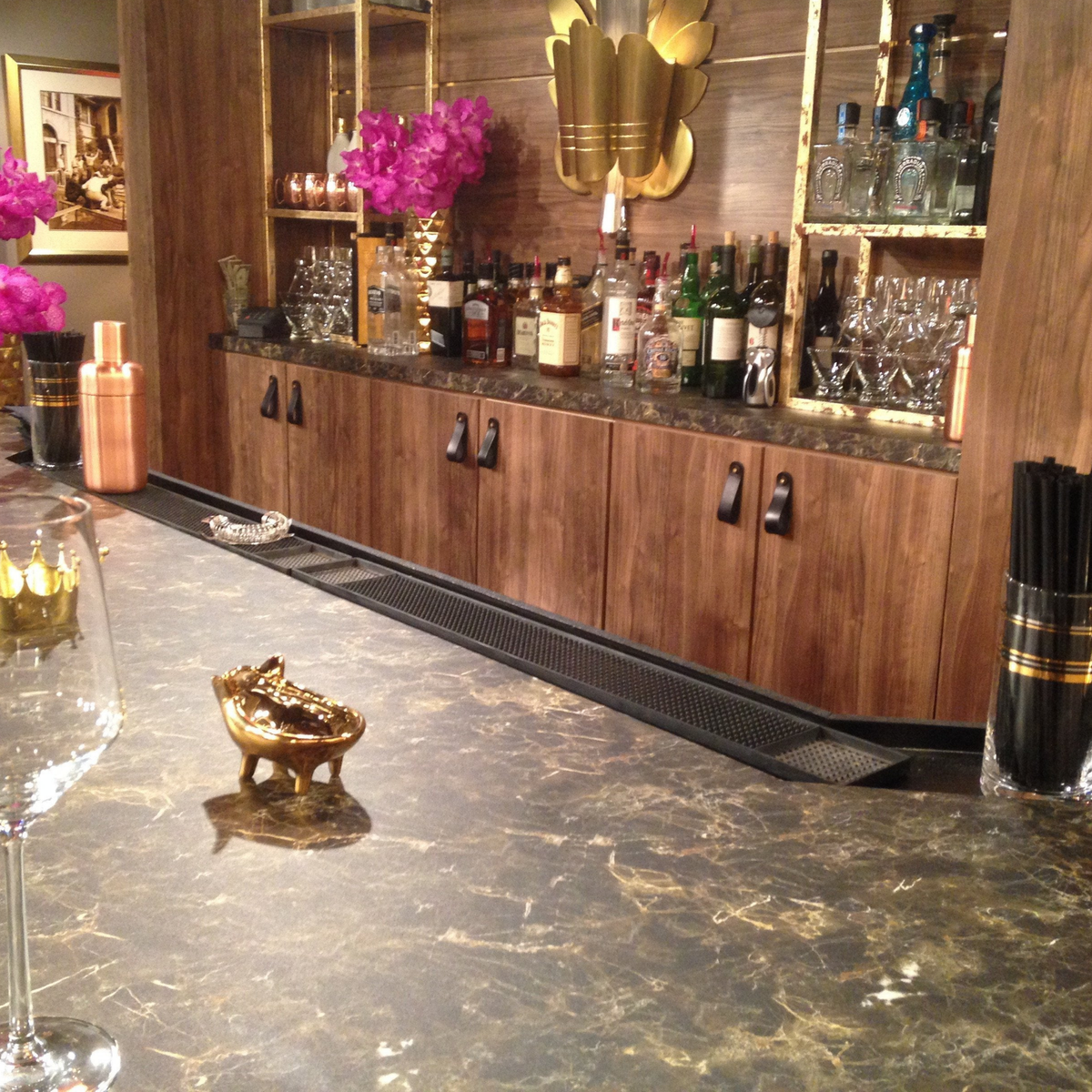 Customer photo of a marble-topped bar on a television show set. Behind the bar is a liquor bottle display with dark wood cabinetry and dark brown leather Hawthorne handles on the cabinet doors. 