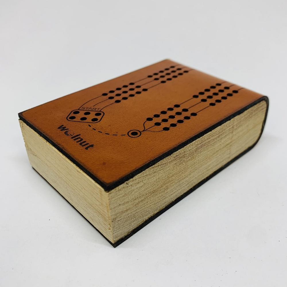 Close-up of Mini Deluxe Travel Cribbage Board on white background, shows the leather surrounds the wood sides with a seam in the middle held closed by magnets. 