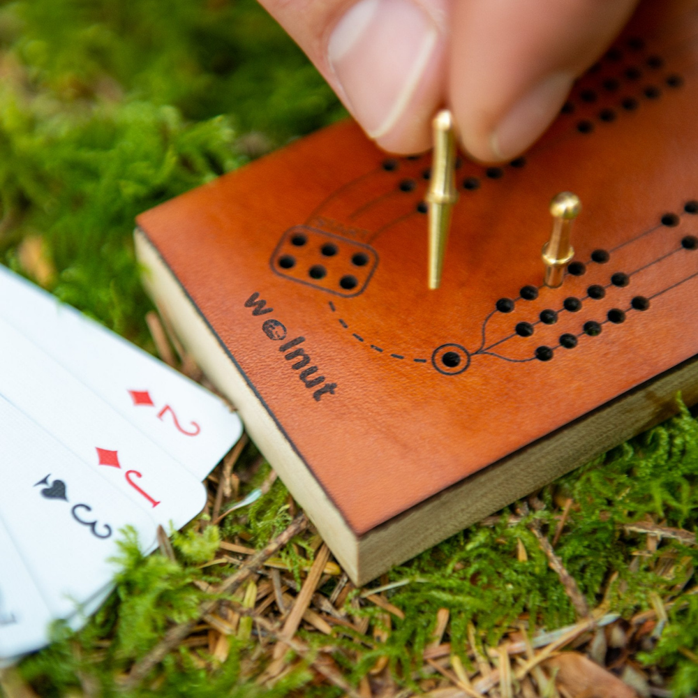 Close-up detail shot showing fine laser-engraving of cribbage board features: three tracks, a winning hole, starting holes, and directional guides. 