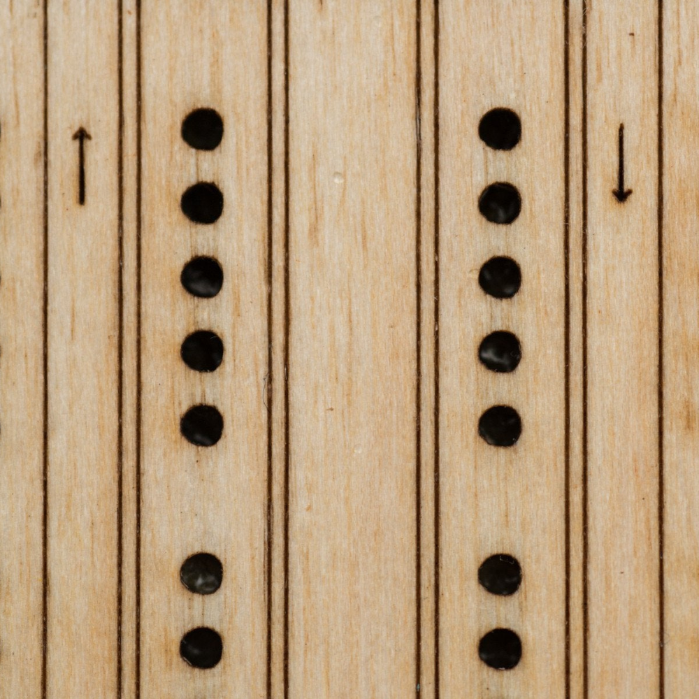 Close-up of laser etched birch playing surface on travel cribbage board, with pegging holes and directional arrows, and a different striping to differentiate the two tracks. 