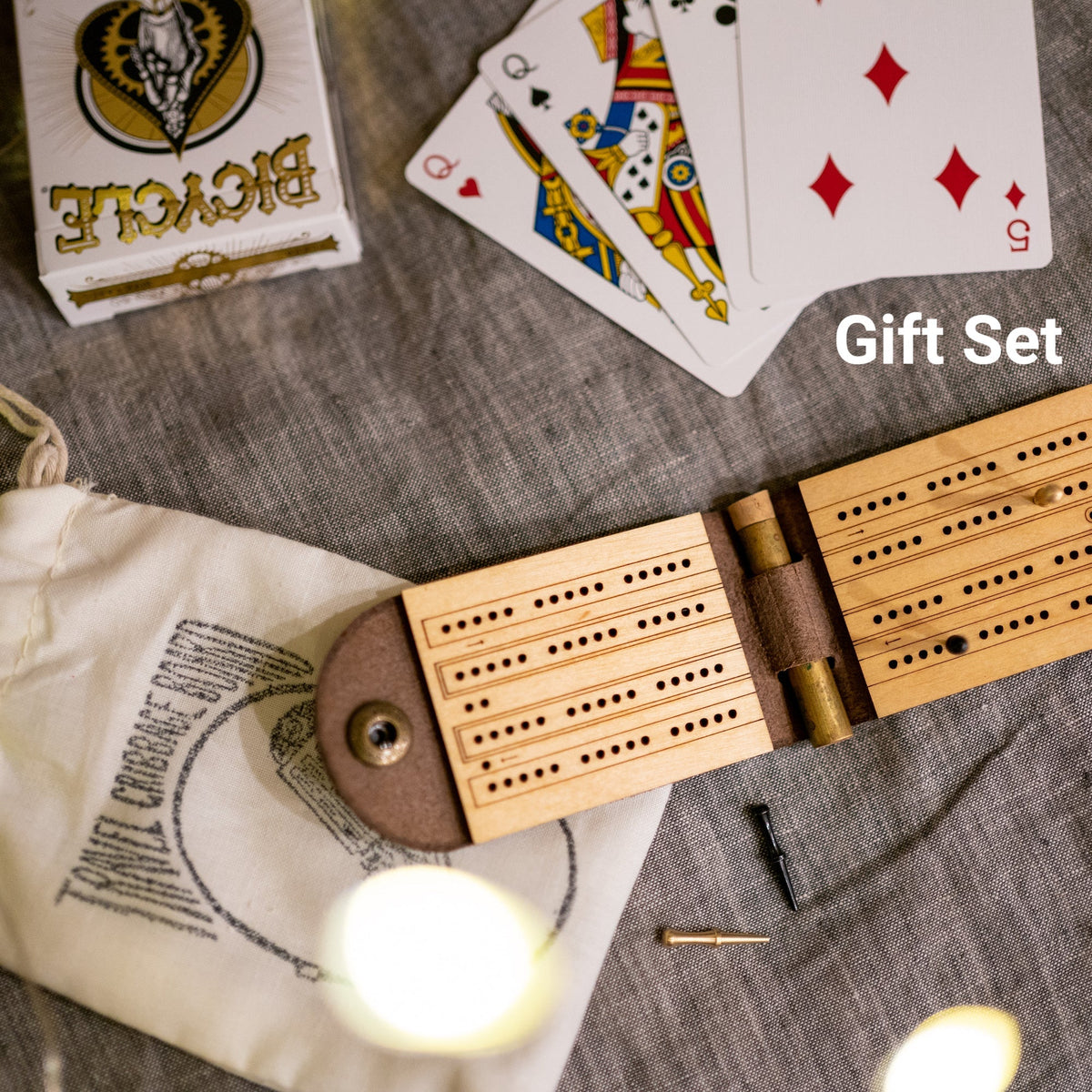 Open leather and wood travel cribbage board with cast metal person on top of a bedspread with a carrying pouch and a deck of cards, which is the &quot;Gift Set&quot;