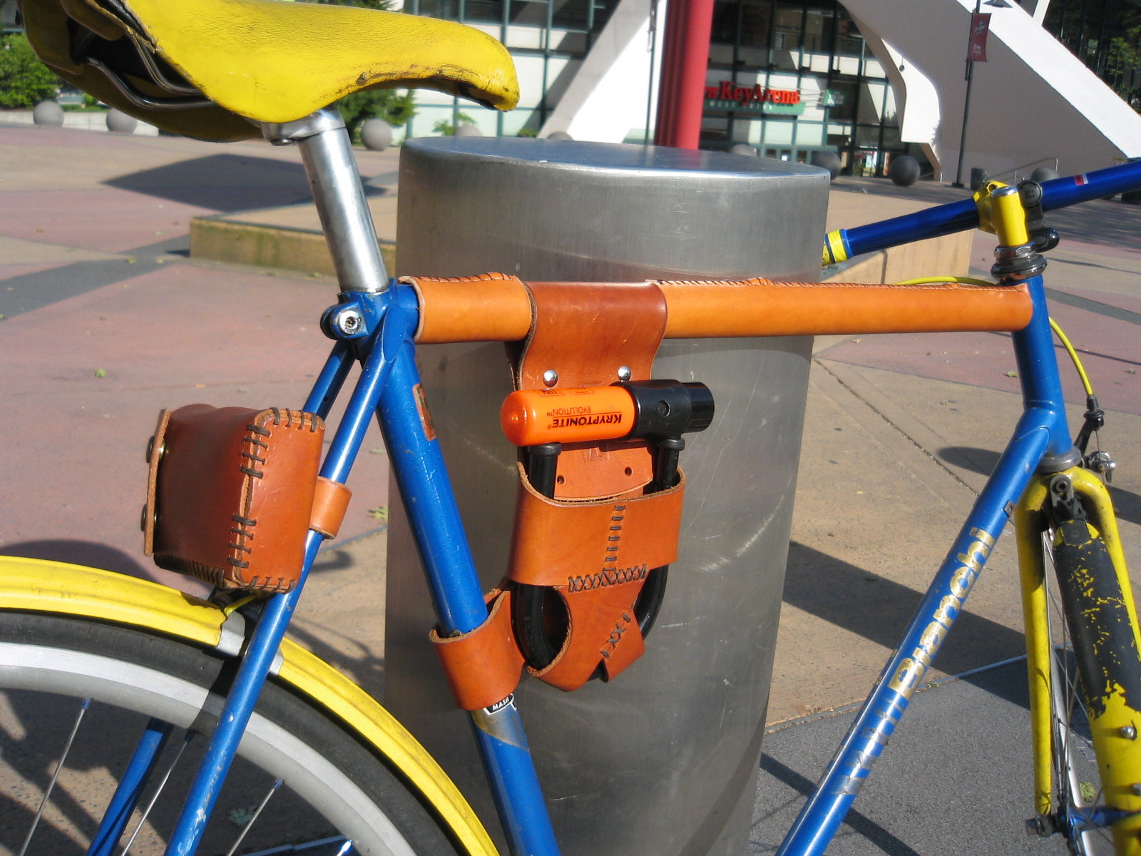 A honey leather bicycle u-lock holster on a bright blue bicycle and a yellow saddle