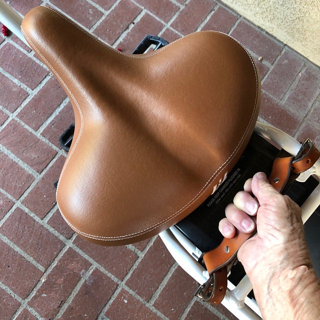 A elderly woman's hand reaching out down to honey leather frame handle on the back rack of her bicycle to help with lifting a heavy bike