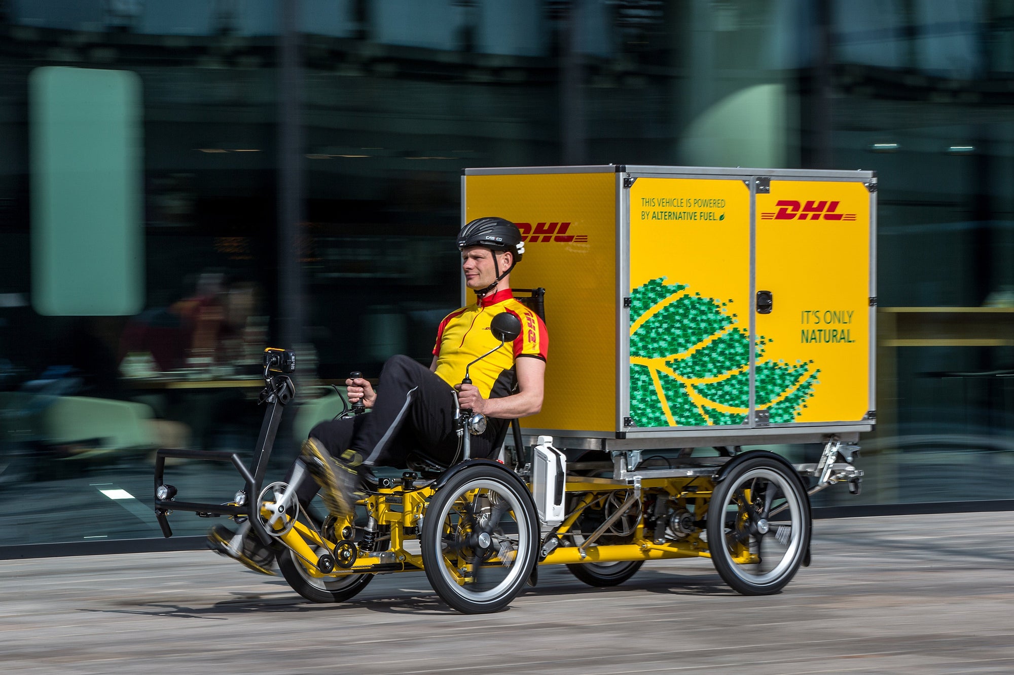 DHL Express delivery person riding a recumbent bicycle delivery with Christmas tree holiday graphics on the trailer