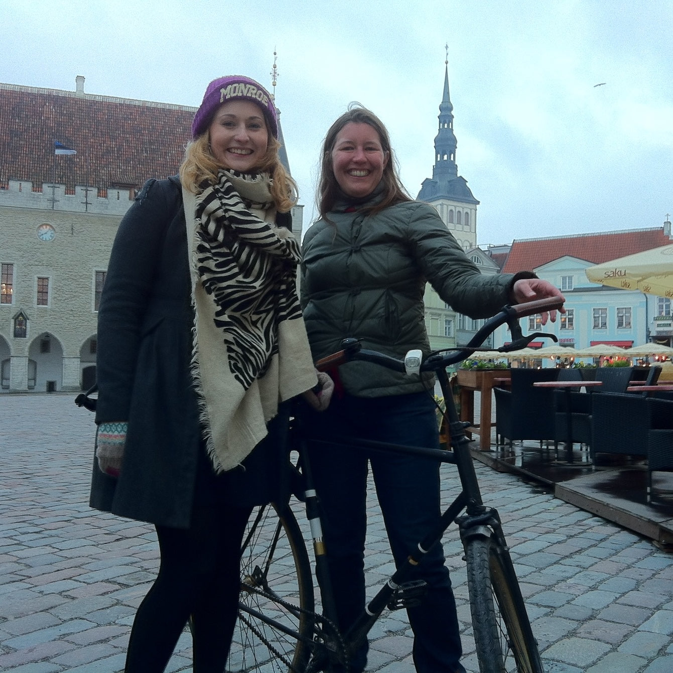 Valerie and an Estonian customer smiling in Tallinn in front of beautiful cityscape and holding her bicycle with leather city bicycle grips