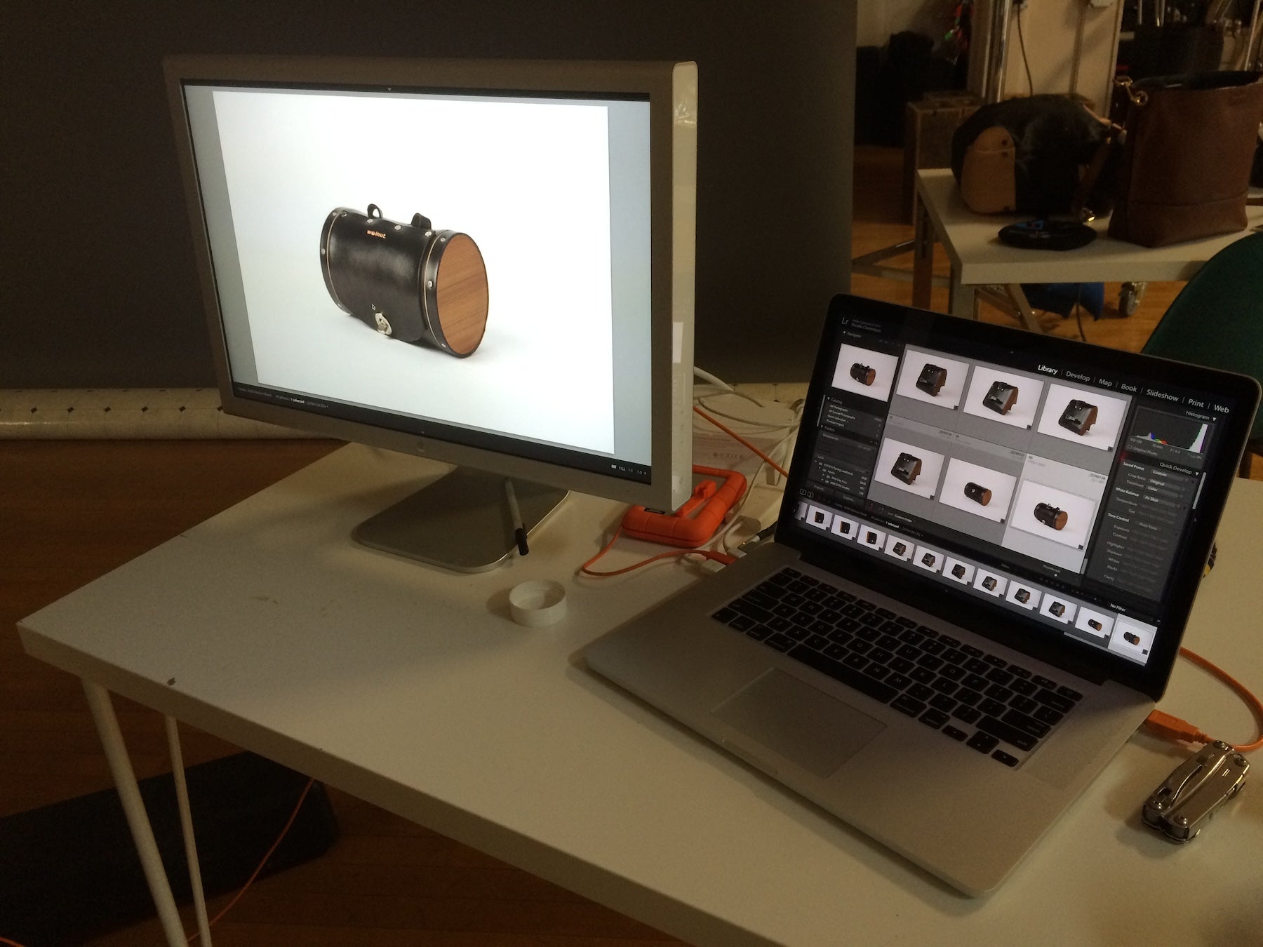 Behind-the-scenes image from a photoshoot of a Walnut Studiolo barrel bag, showing the photographer's work station with a large monitor showing the Black Seat Barrel Bag, and the laptop with the working image program