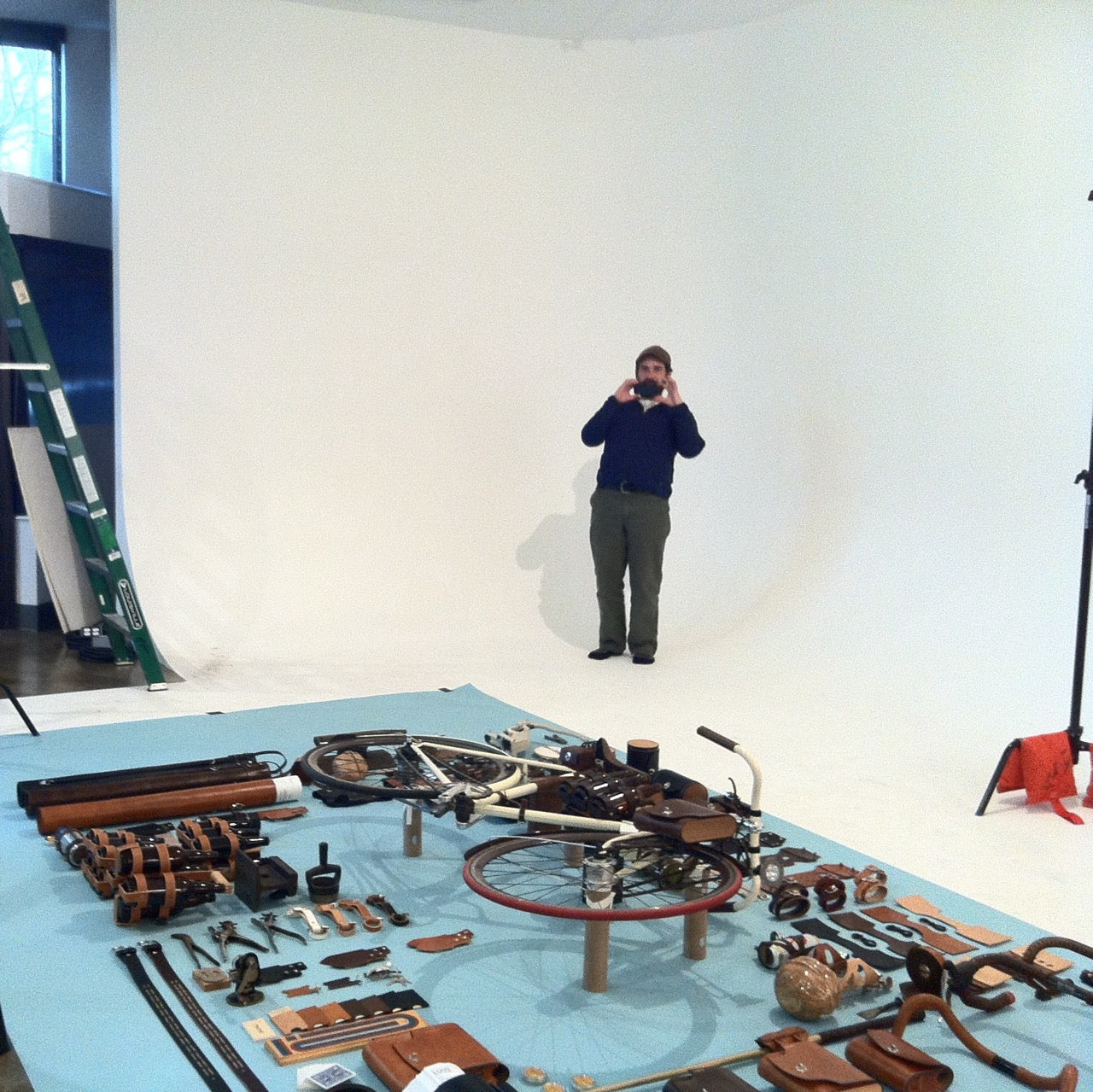 A man in a photo studio is standing back in front of a white backdrop and taking a photo of a large art project on the ground in front of him