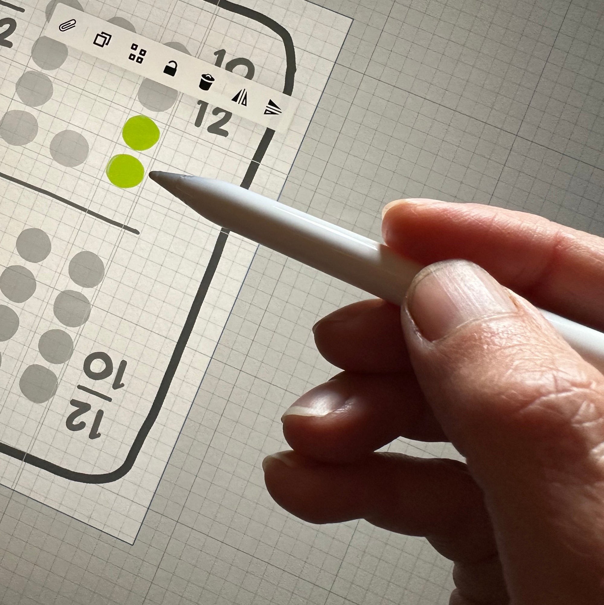 A woman's hand is holding a digital Apple Pencil over a tablet and drawing a domino playing card on the screen