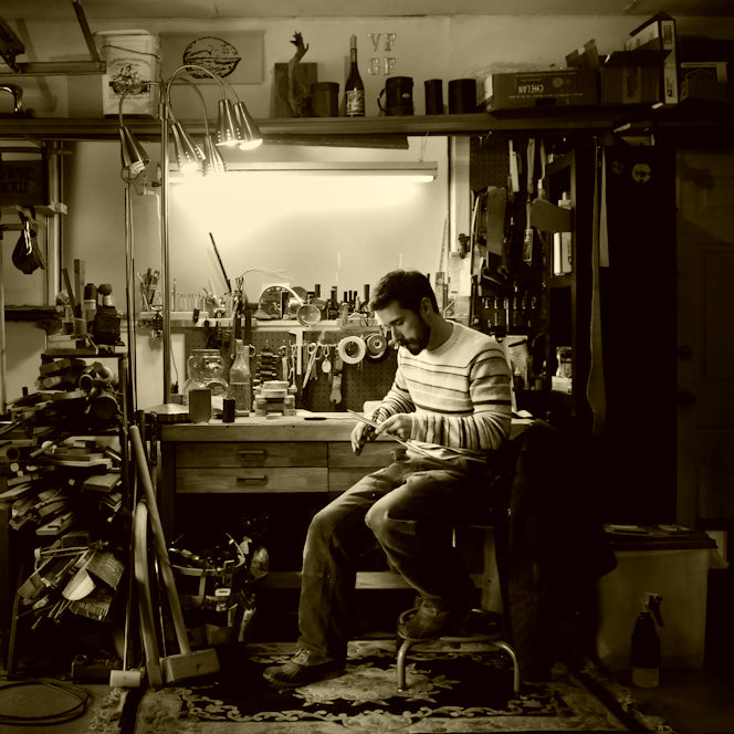 A sepia-toned photo of Geoff working in a cozy corner of the workshop at a bench underneath under a focus light. Image credit: Russ Roca, Path Less Pedaled