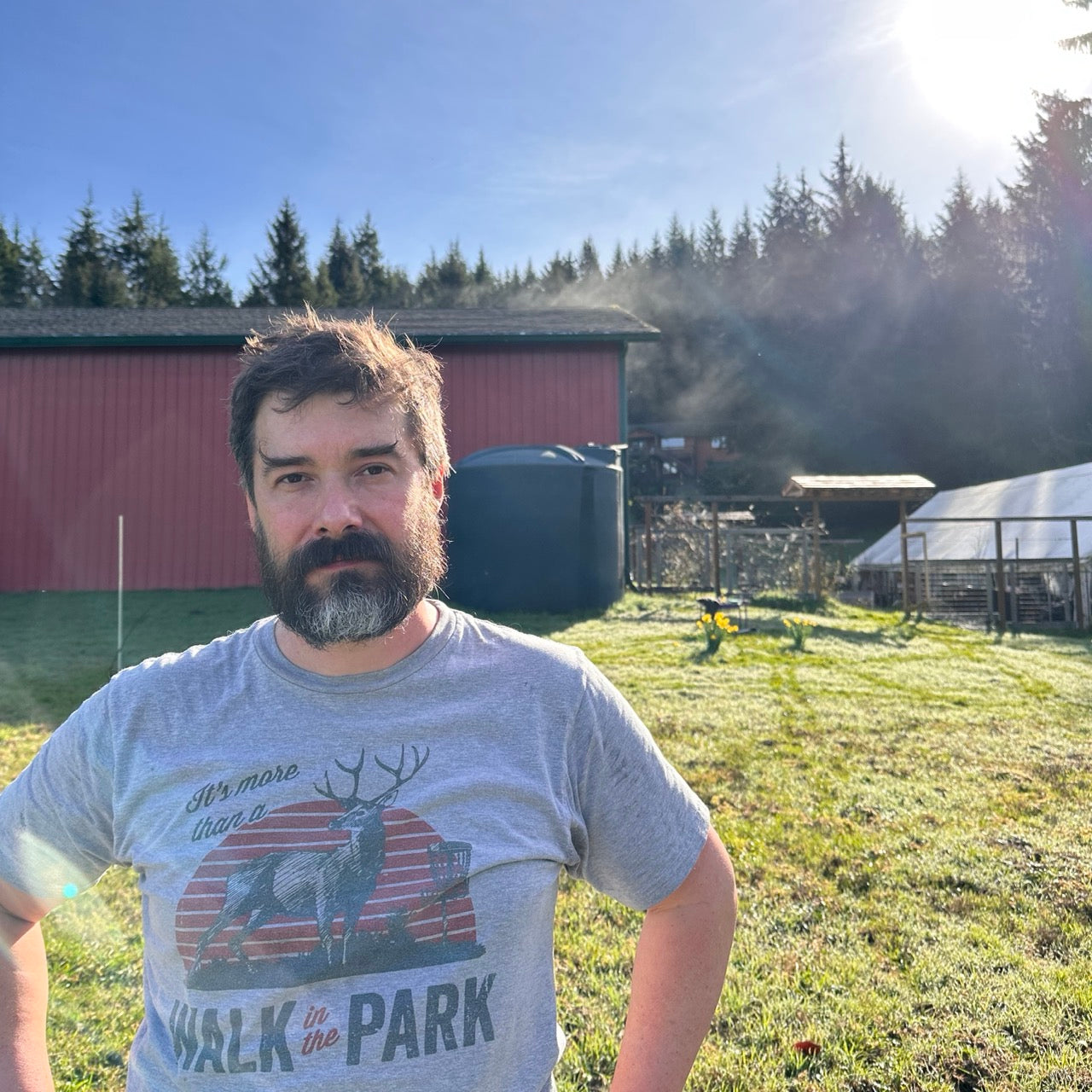 Geoff standing in front of the workshop, rainwater tank greenhouse and garden orchard