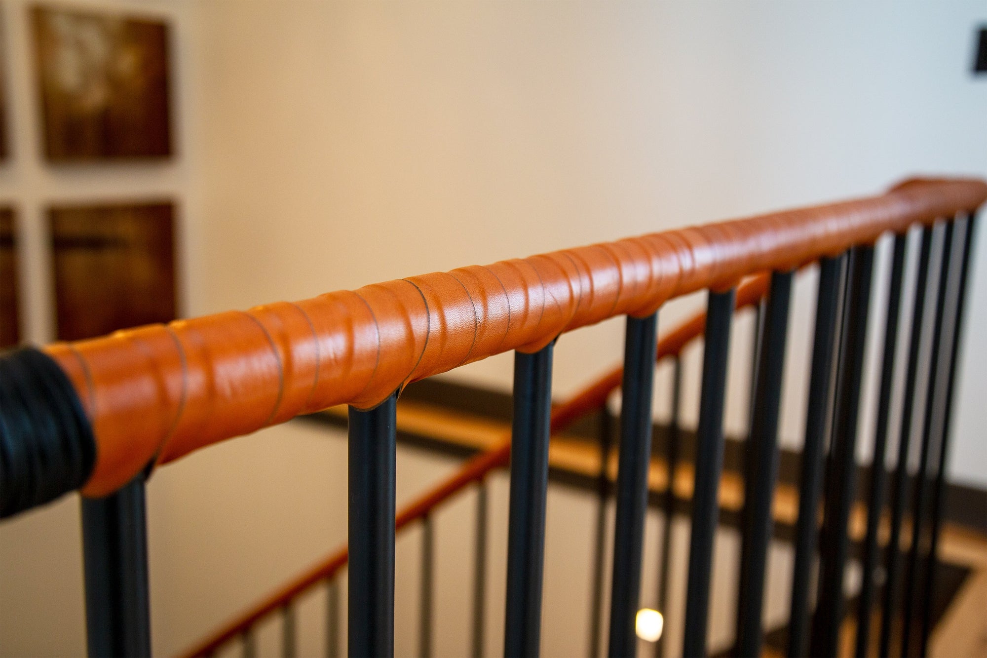 A black metal bannister or stairway railing in a hallway, with the top bar wrapped in wide coils of honey American vegetable-tanned hand-dyed real leather