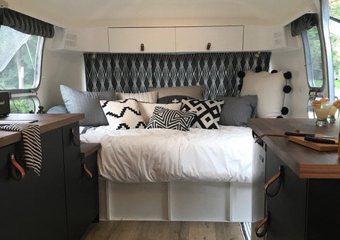 Inside the Airstream in the middle of the galley kitchen, looking to the back of the bus where the bed / couch is. There is a strong design theme of black and white textiles with honey leather and walnut wood accents, and Hawthorne Small leather loop hand