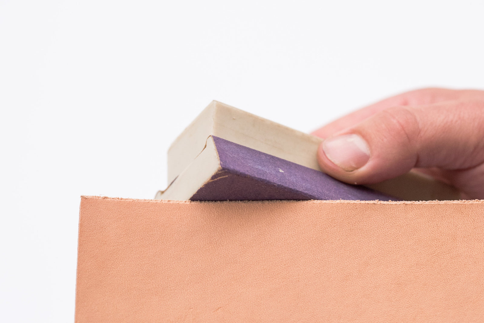 Sanding the edge of a piece of leather using a fine grit piece of sandpaper