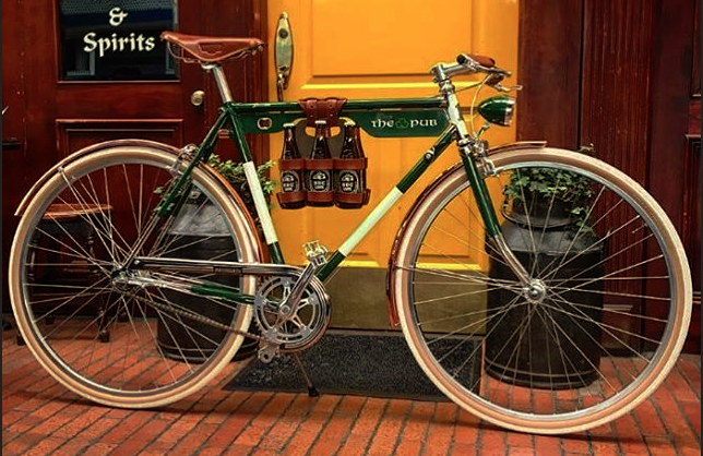 A handsome kelly green bicycle custom built for an Irish pub, parked in front of a bright yellow door with honey leather bicycle accessories