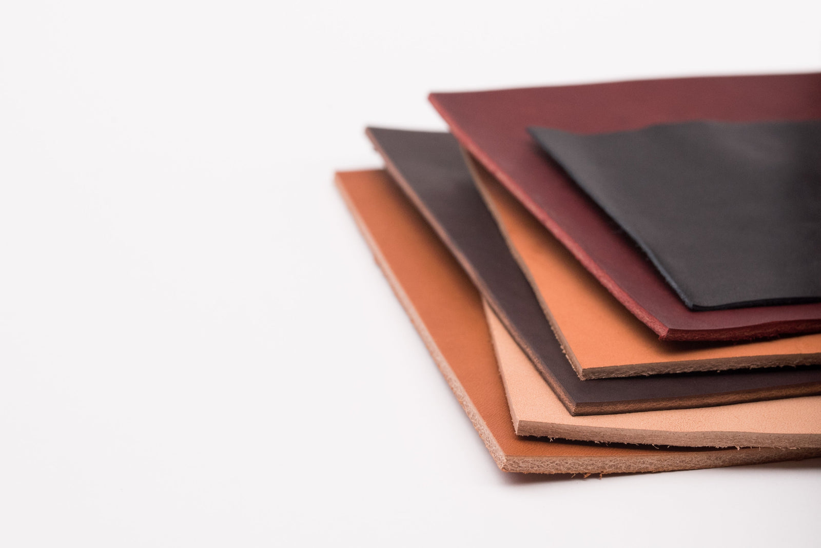 A stack of several pieces of leather in different colors and tannages on a white background