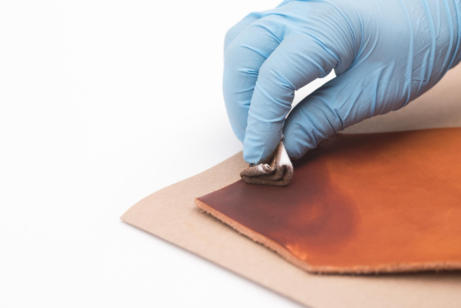 A gloved hand rubbing in oil dye to a piece of full grain veg-tan leather