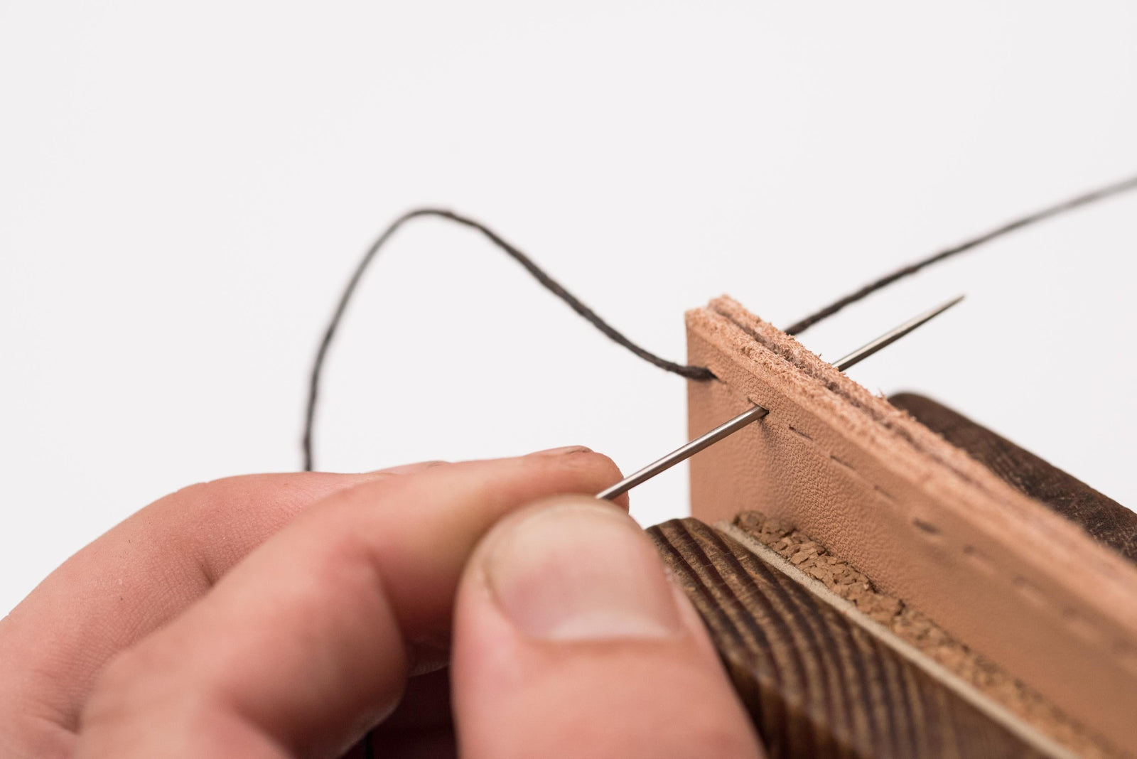 Close-up of a man stitching together two layers of leather on a stitch horse