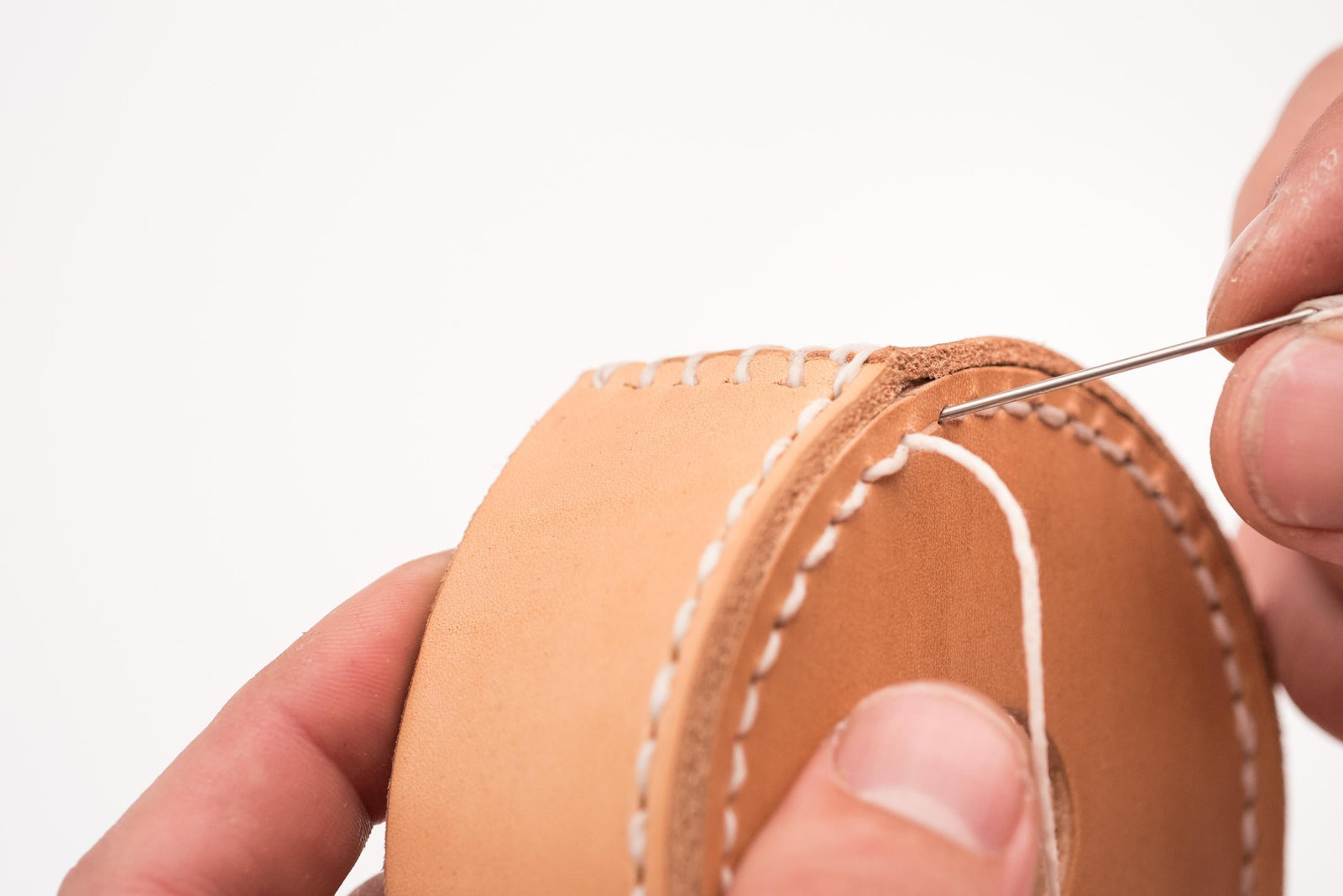 Close-up of hand stitching together a round leather cap with stitching in three directions