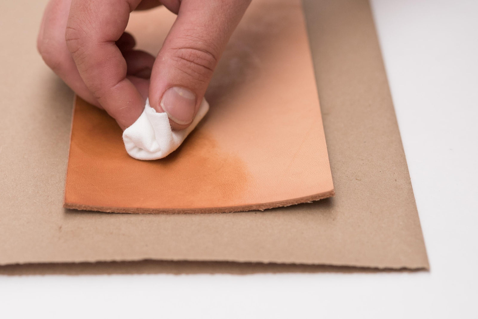 A hand rubbing a clear gloss onto a piece of natural leather