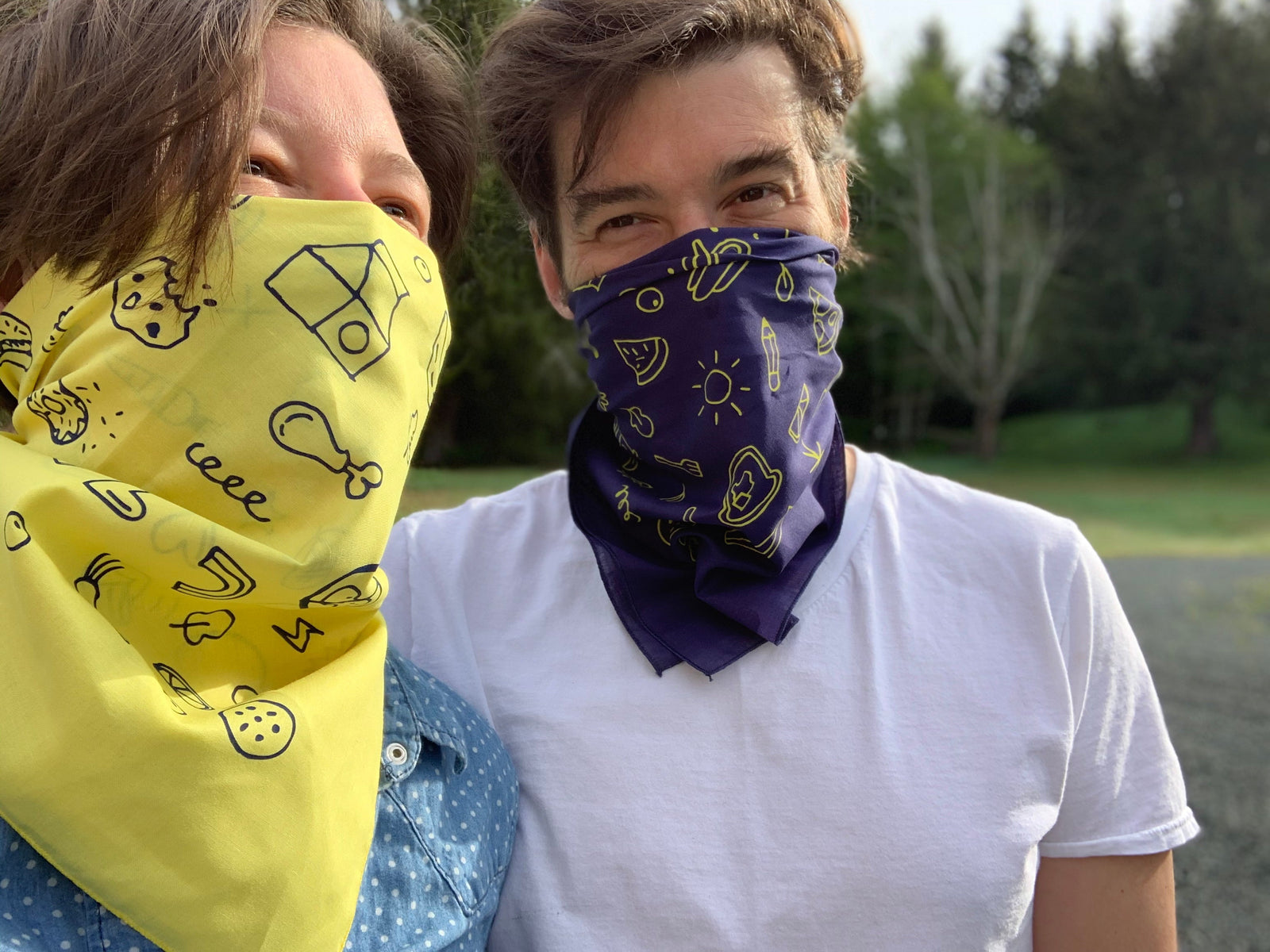 Valerie and Geoff wearing complementary yellow and blue bandanas like face masks and smiling against a forest backdrop