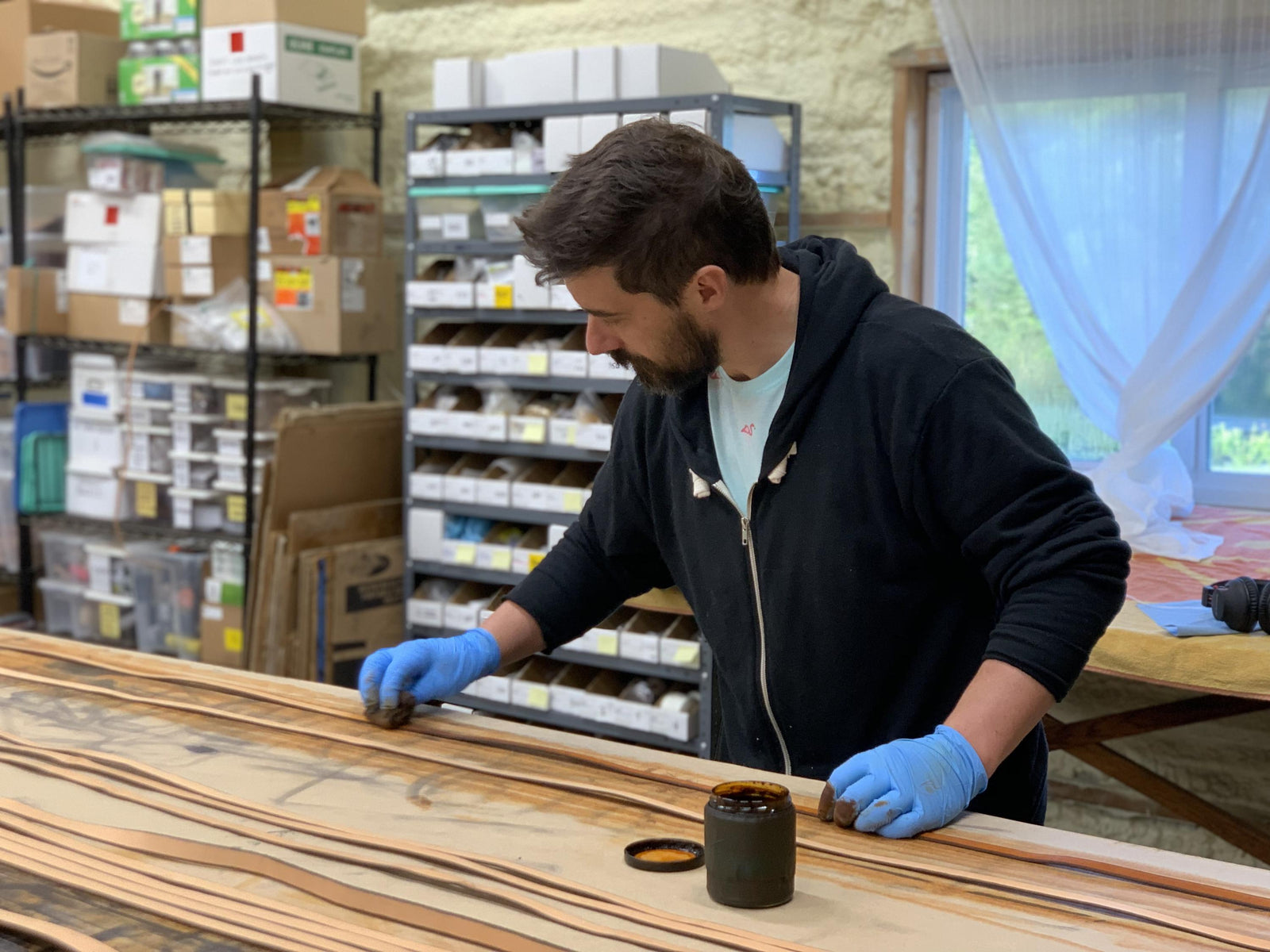 A man at a workbench, applying dye to leather straps with blue gloves on