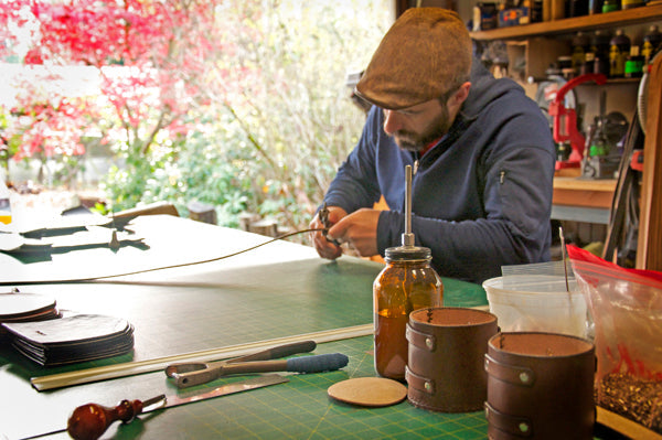 A leathercrafter leaning over a work bench with a hand tool