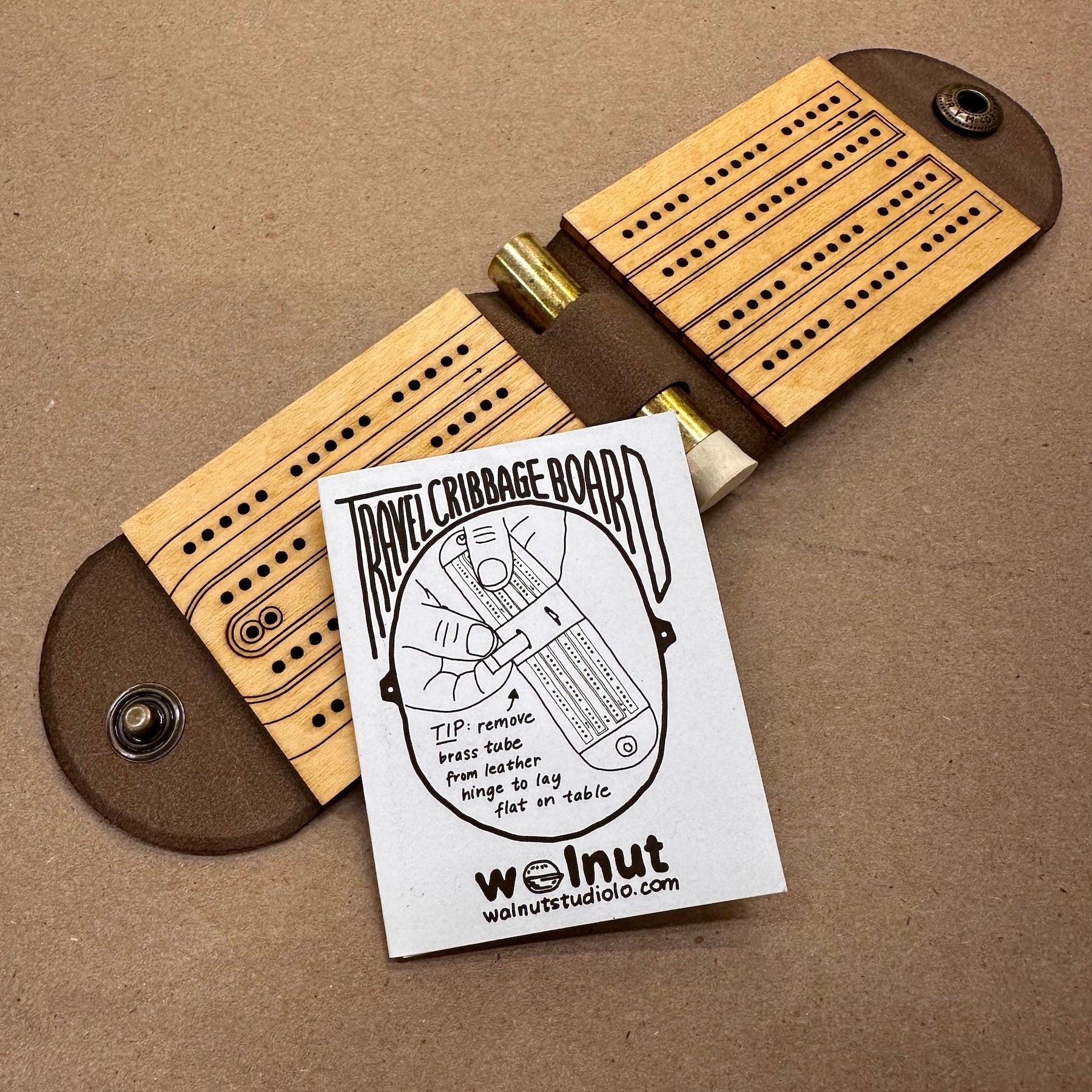 A leather folding travel cribbage board with a small white hand-drawn rules booklet 