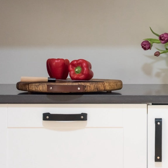 A clean kitchen with white cabinets and leather Tilikum handles in three colors on the cabinets and the cutting board