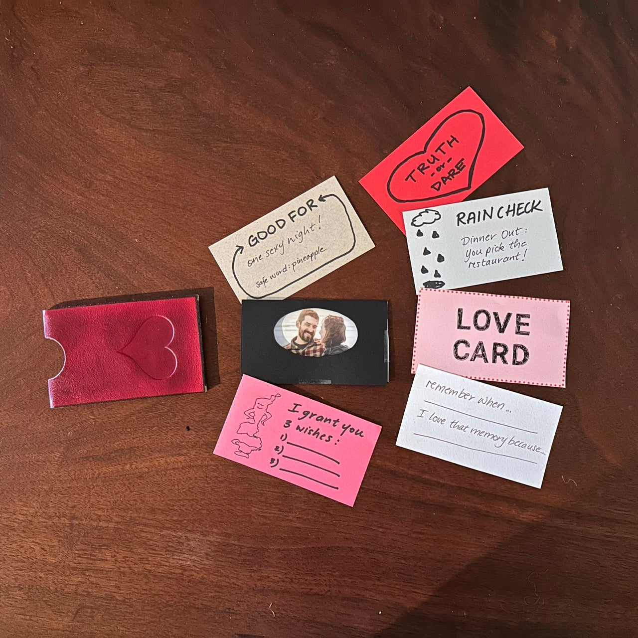 Collection of small DIY love note cards and a mini photo on a wooden surface with a love edition red leather business card case on a walnut wood table
