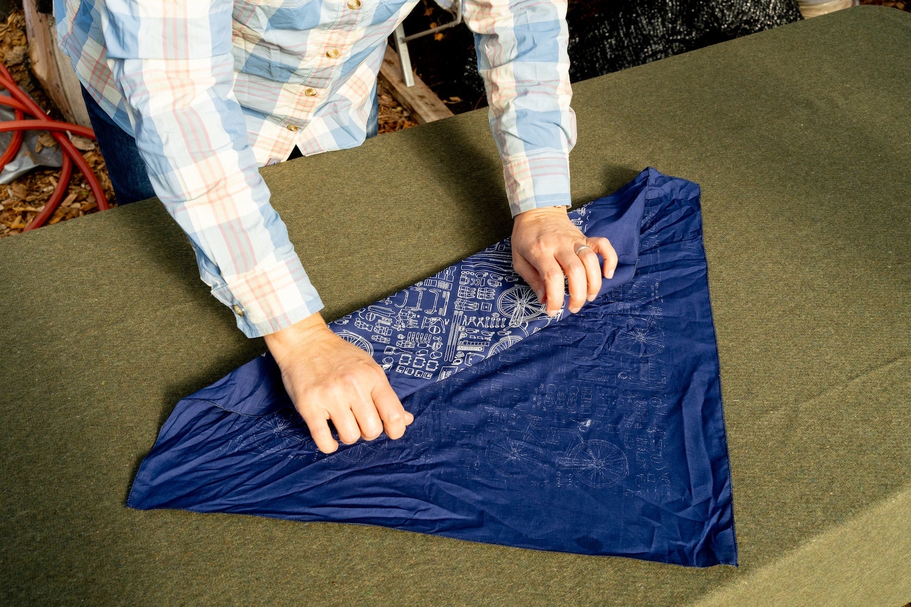 A woman standing over a table, gift-wrapping an item in a bandana, folding the cloth